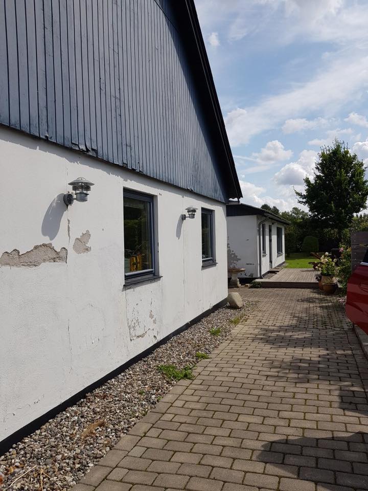 Hus med slidt og afskallet hvid facade langs brolagt indkørsel – eksempel på bygning før renovering.