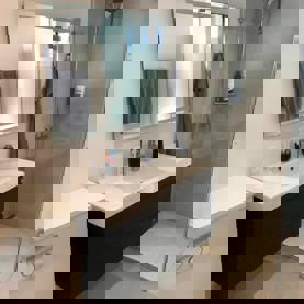 Lyst badeværelse med væghængt vaskeskab, bruseniche og lyse gulv- og vægfliser som eksempel på professionel opsætning af klinker.