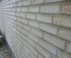 Ny opmuret mur i lyse teglsten med grå fuger, set langs husets facade.