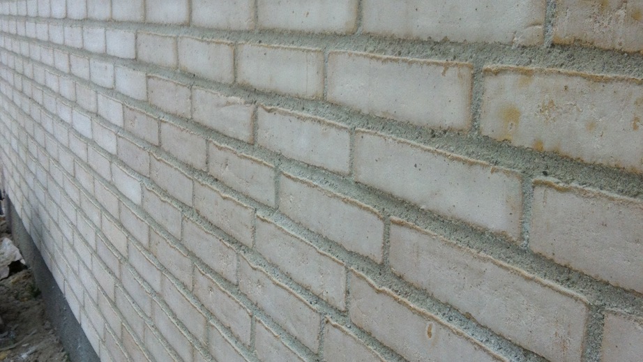 Ny opmuret mur i lyse teglsten med grå fuger, set langs husets facade.