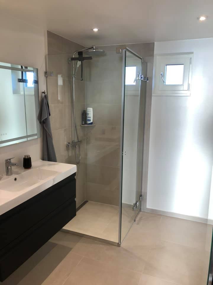 Moderne badeværelse med glasafskærmet bruseniche og lyse væg- og gulvfliser, der viser flot opsætning af klinker.