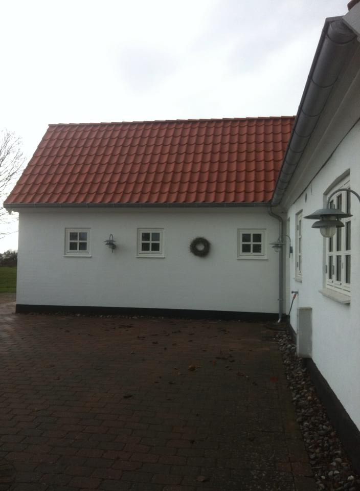 Hvid landejendom med rødt tegltag, små sprossede vinduer og brolagt gårdsplads set fra gårdsiden.