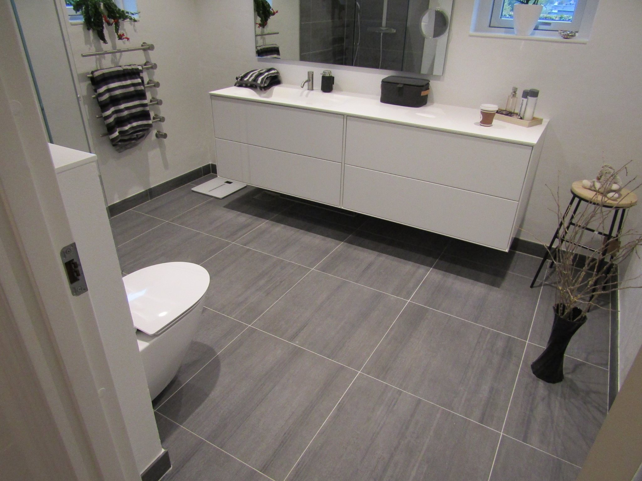 Moderne badeværelse med store grå gulvklinker og hvidt inventar, der viser eksempel på professionel opsætning af fliser og klinker.