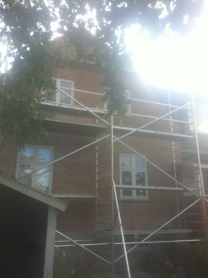 Murstenshus med opstillet facadestillads under renovering, set udefra i modlys.