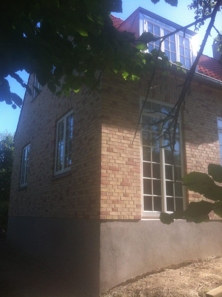 Renoveret murstenshus med pudset sokkel og store vinduer - set fra siden i sollys.